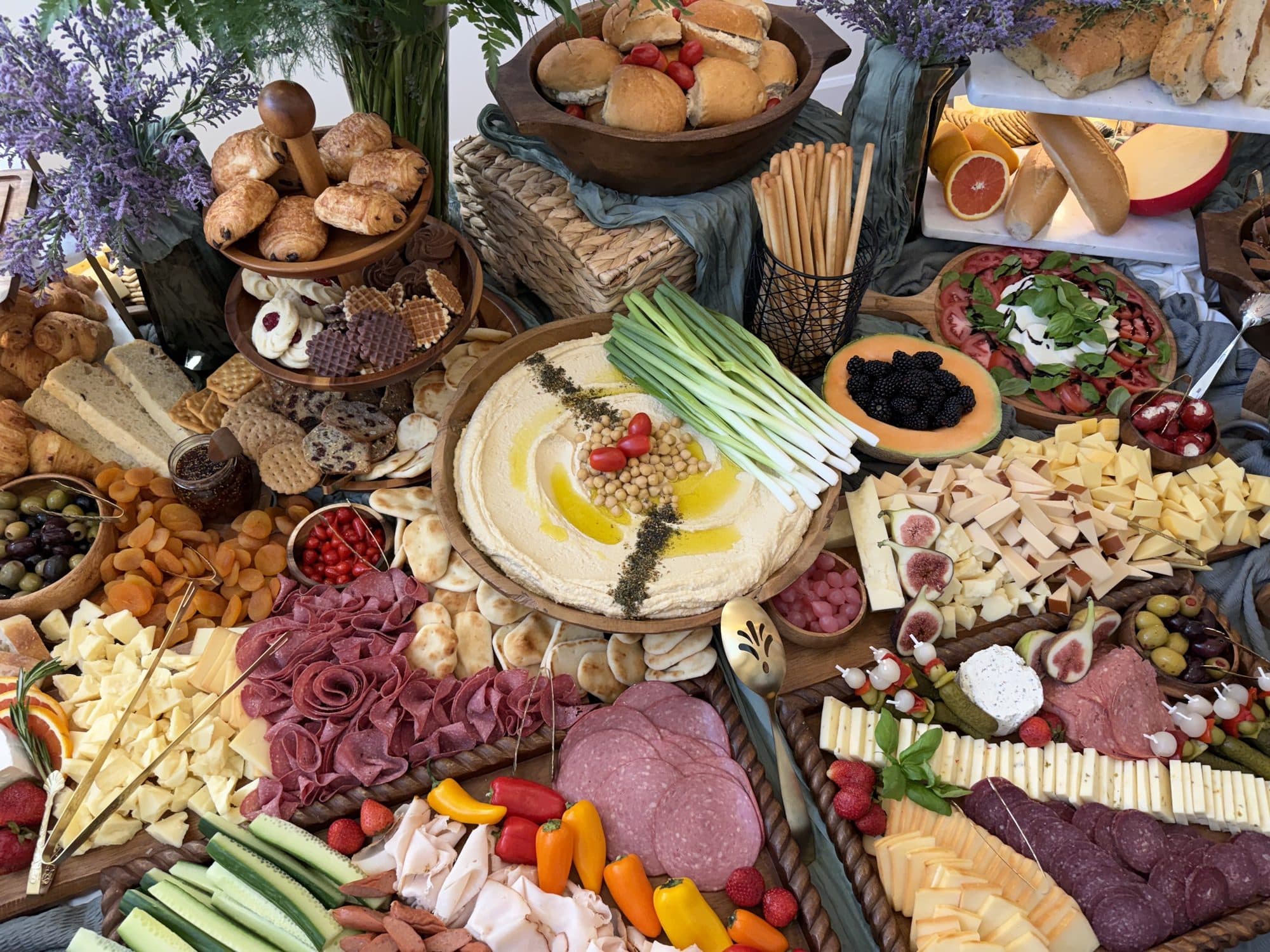 Hummus with chickpeas and green onion at the centre of a board of cheeses, charcuterie and fresh vegetables