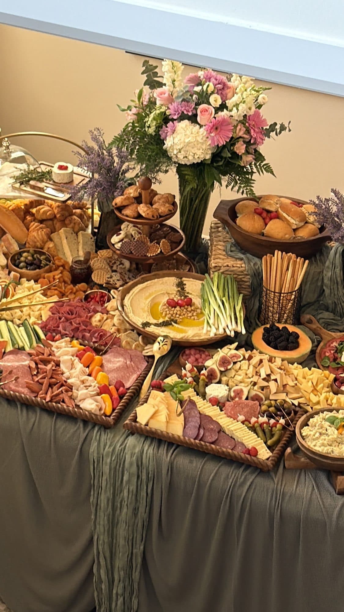 A grazing table styled by The Orchid Touch, with a pink and white floral arrangement rising above breads, hummus and charcuterie